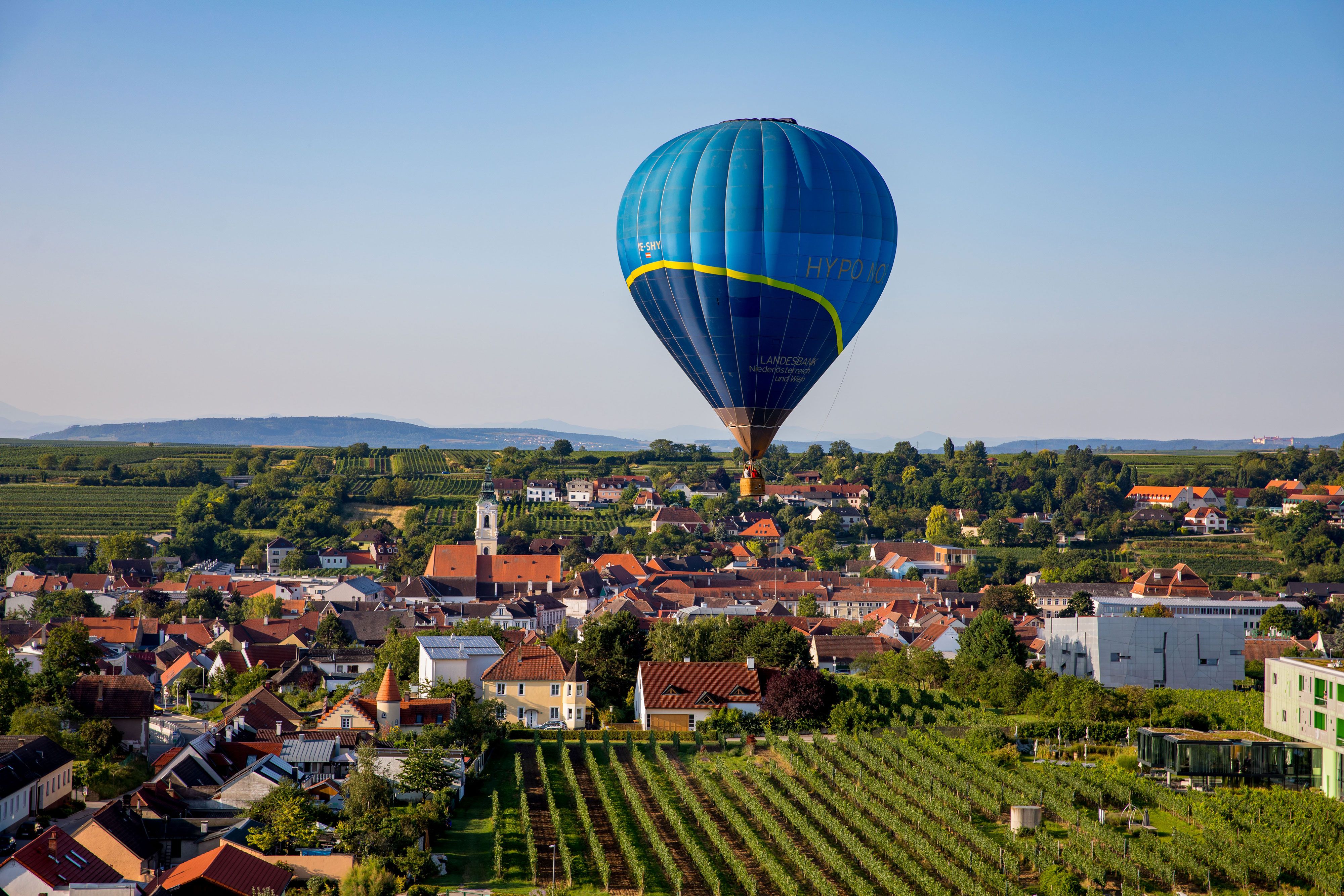 Heißluftballon über einer Stadtlandschaft mit Weinbergen und Häusern.