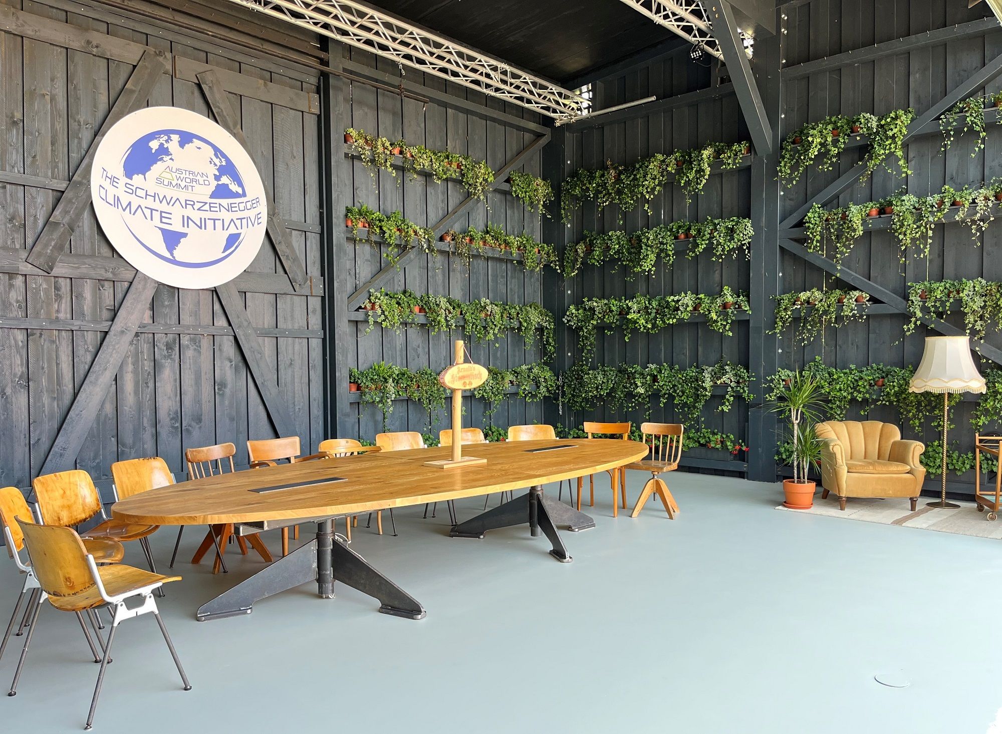 Ein moderner Besprechungsraum mit Holztisch, Stühlen und Pflanzen an den Wänden. Ein Logo der Schwarzenegger Climate Initiative ist sichtbar.
