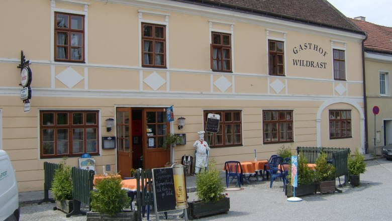 Gasthof Wildrast, © Gasthof Wildrast Außenansicht des Gasthofs Wildrast mit Tischen und Stühlen im Freien.