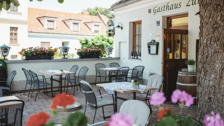 Schattiger Gastgarten mit Tischen und St&uuml;hlen vor einem Gasthaus.
