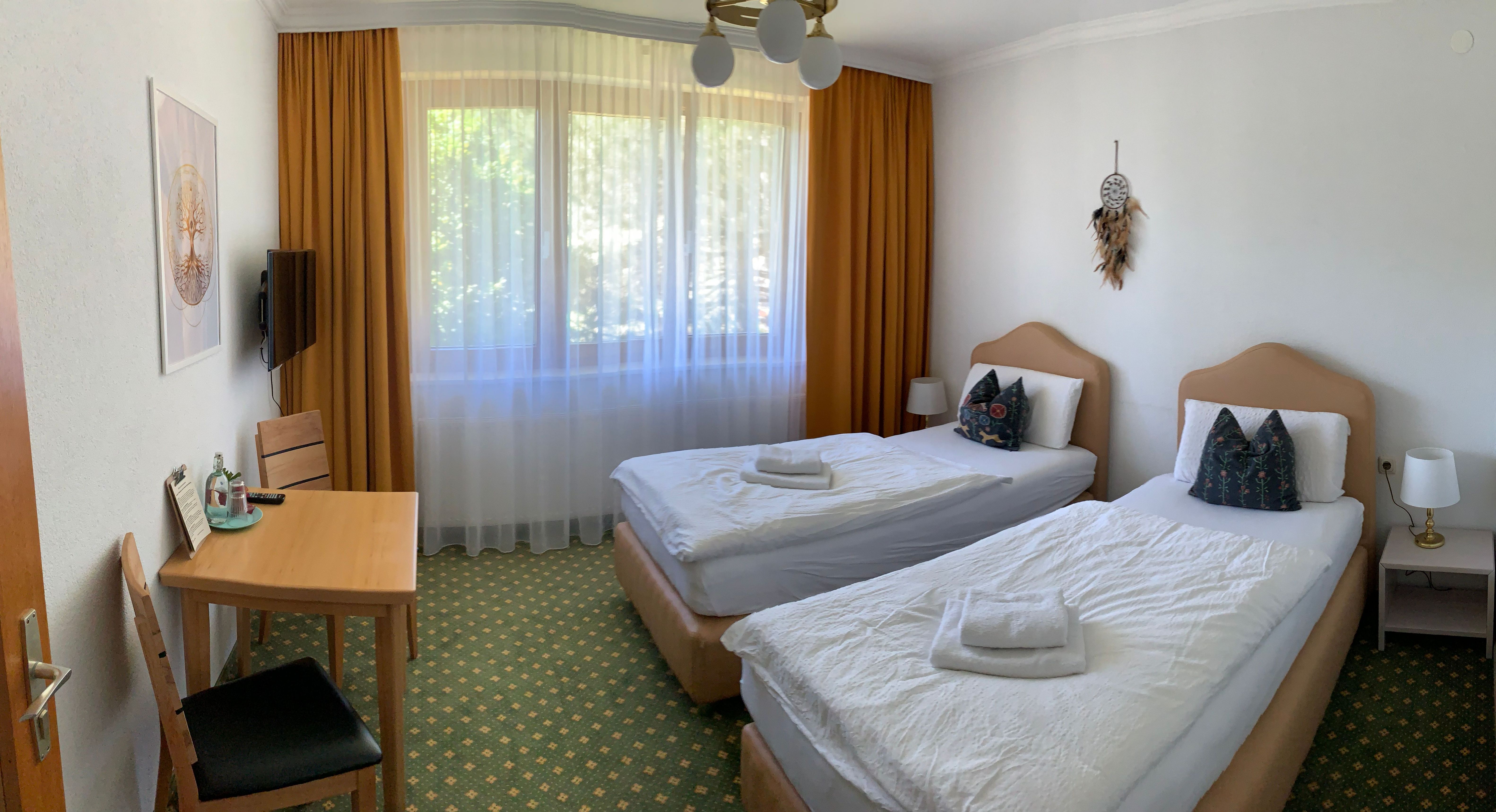 Ein Hotelzimmer mit zwei Einzelbetten, einem Tisch mit Stühlen und einem Fenster mit Vorhängen.