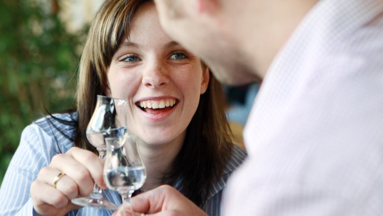 Zwei Personen sto&szlig;en mit Schnapsgl&auml;sern an und l&auml;cheln.