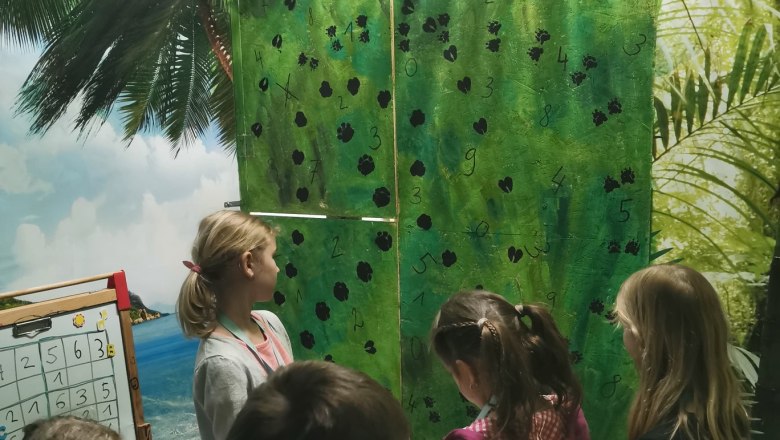 Kinder stehen im Raum und lesen ein Rätsel