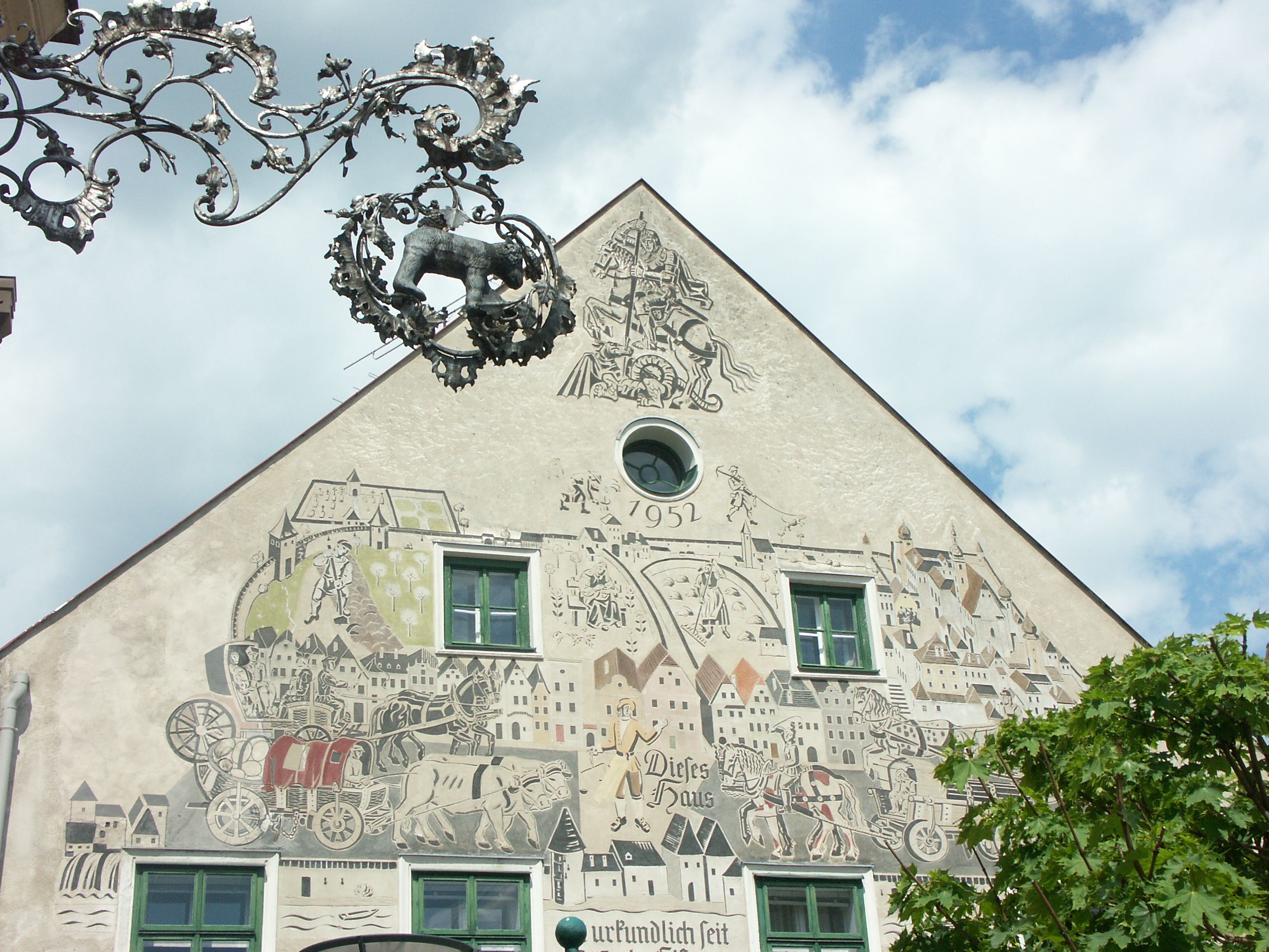 Fassade eines Hauses mit Sgraffito-Kunstwerk und dekorativem Metallschild.