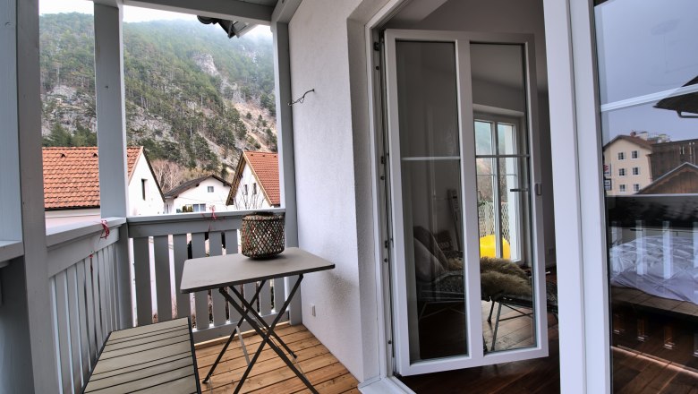 Ein Balkon mit Tisch und Bank, umgeben von Bergen und H&auml;usern mit roten D&auml;chern.