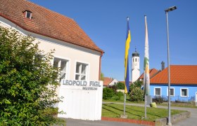 Leopold Figl Museum mit Fahnen und Kirchturm im Hintergrund.
