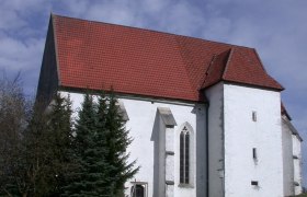 Andreaskirche in Kirchberg an der Pielach mit rotem Ziegeldach und weißer Fassade, umgeben von Bäumen und einem Weg im Vordergrund.
