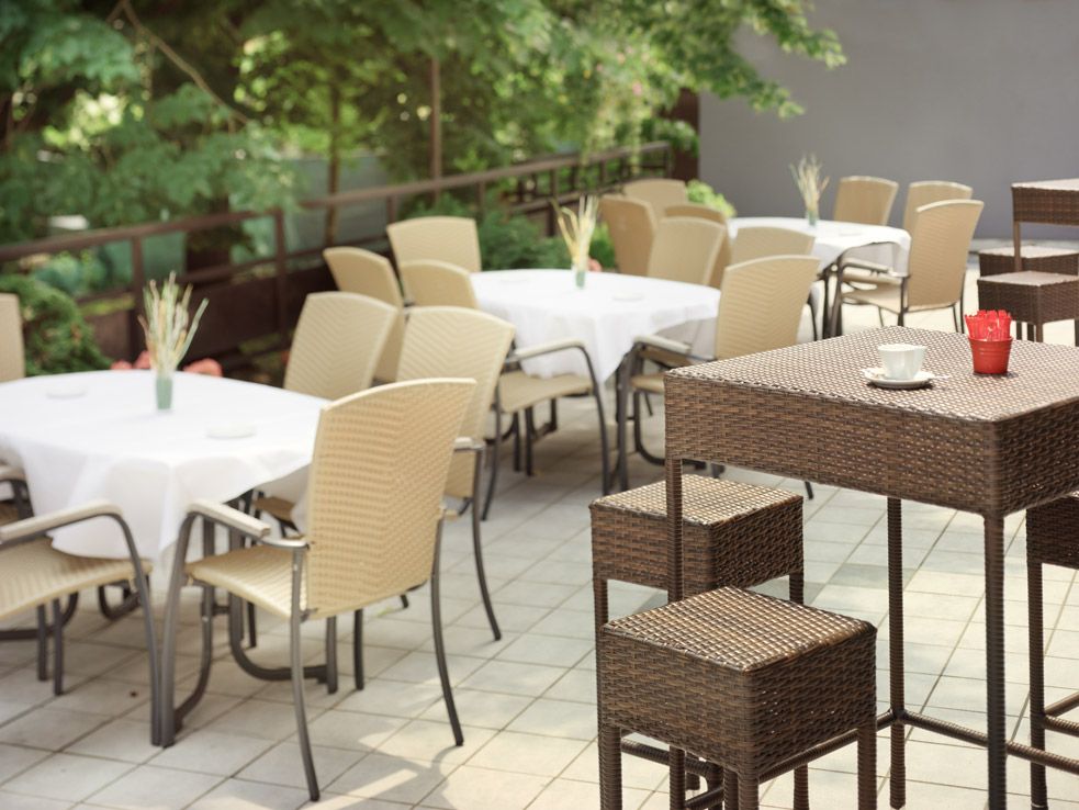 Terrasse mit Tischen und Stühlen, umgeben von grünen Bäumen.