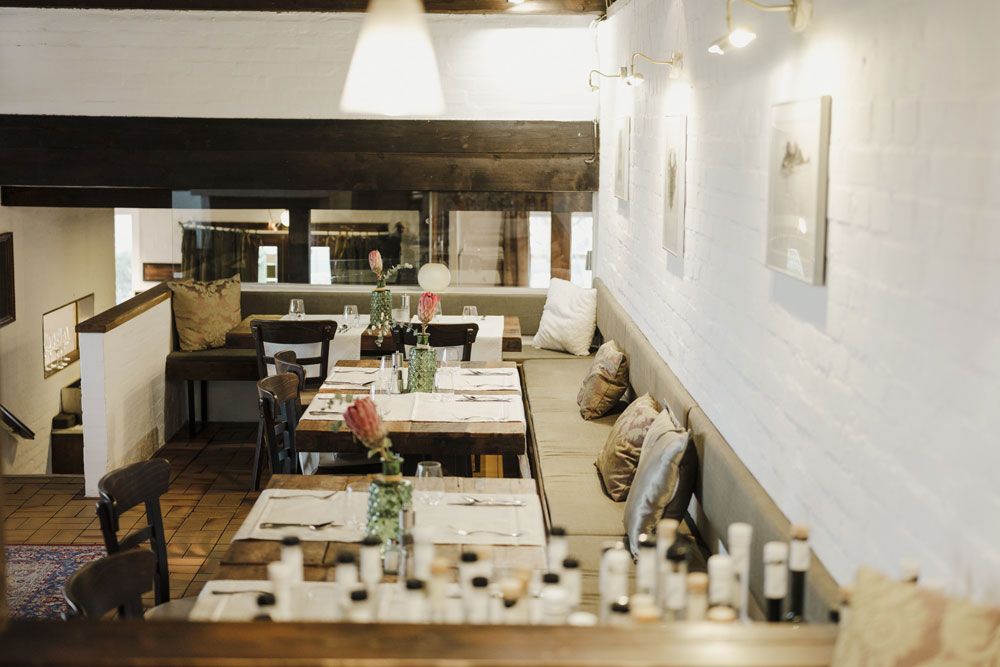 Gemütliches Restaurant mit Holztischen, Kissen und dezenter Beleuchtung.