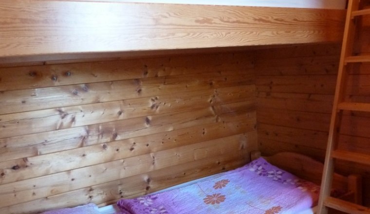 Innenansicht eines Holzferienhauses mit Etagenbett und lila Bettw&auml;sche.