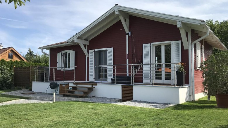 Haus gartenseitig, © Familie Mokesch Ein rotes Holzhaus mit weißem Dach und Fensterläden, umgeben von einem gepflegten Garten.