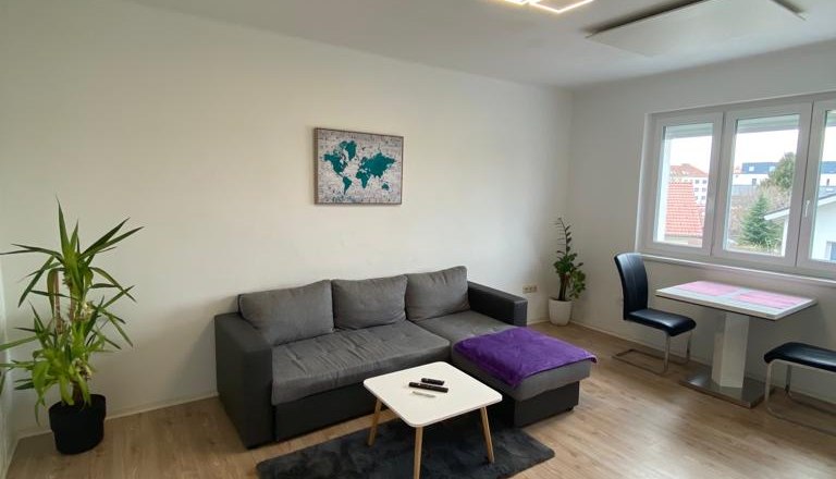 Wohnzimmer mit Couch und Bildern an der Wand sowie gro&szlig;em Fenster