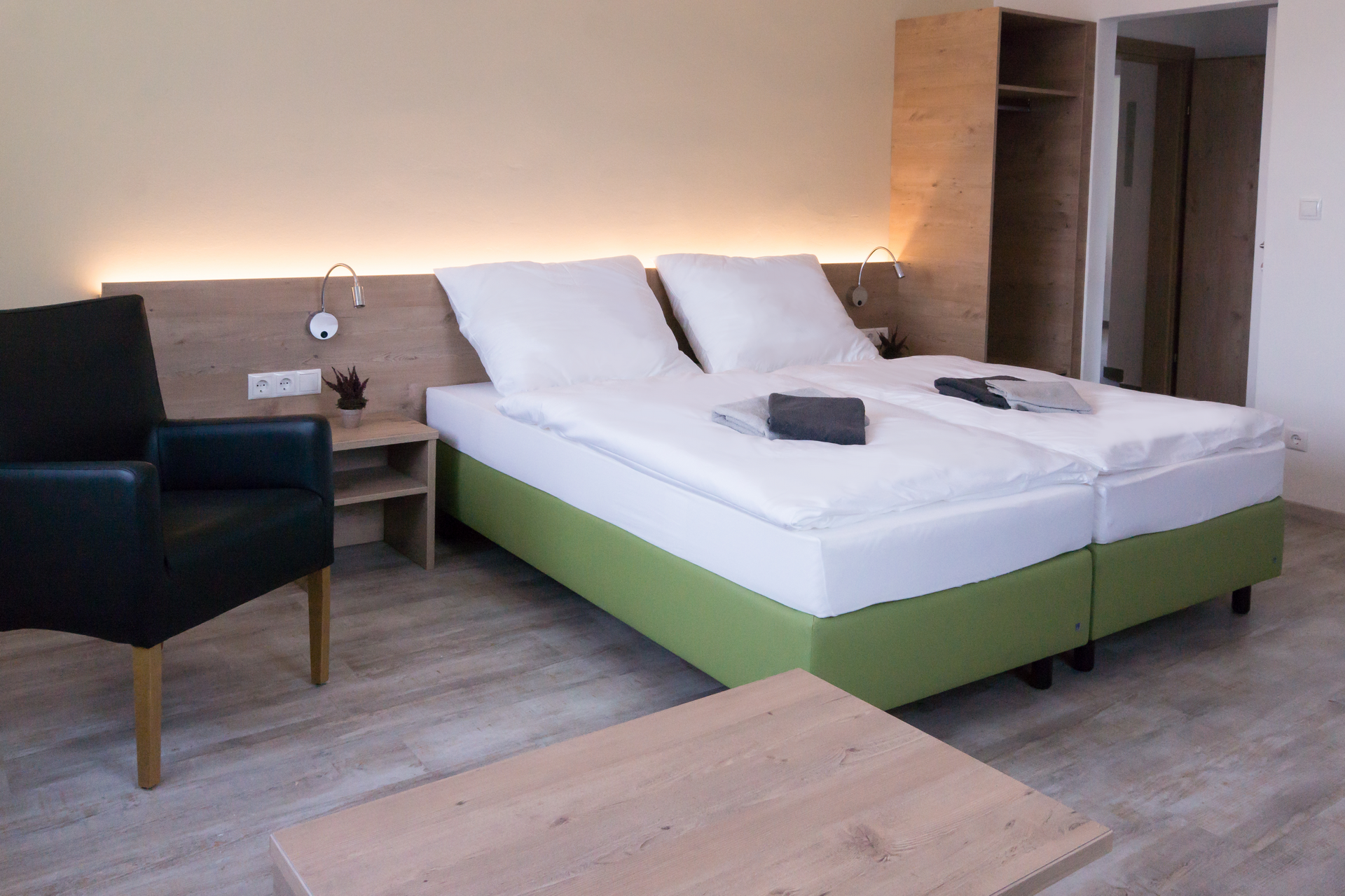 Modern eingerichtetes Hotelzimmer mit Doppelbett, Nachttisch, Sessel und Kleiderschrank.