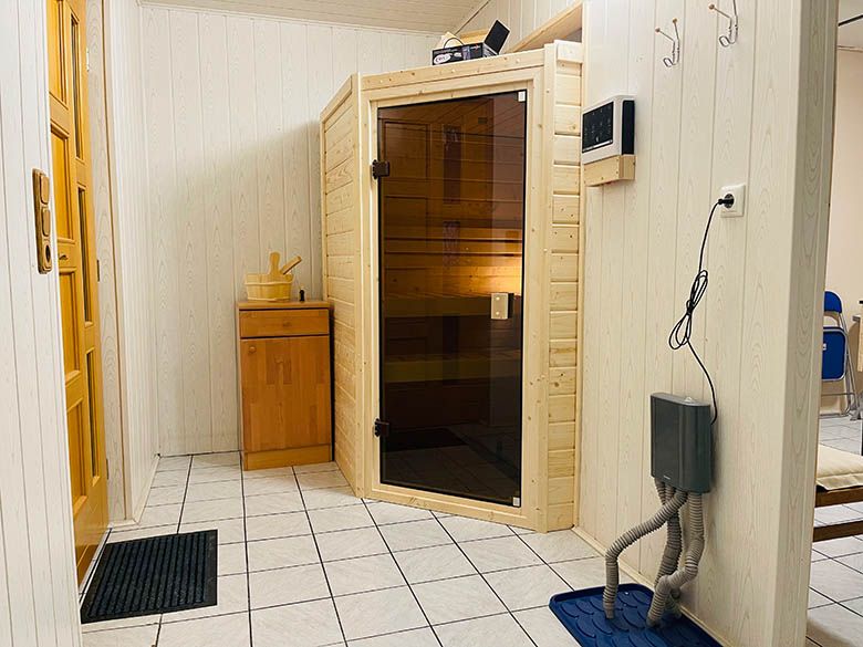 Innenansicht eines Saunaraums mit Holzwänden, einer Glastür und einem kleinen Holzschrank.