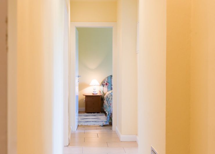 Ein heller Flur führt zu einem Schlafzimmer mit Nachttischlampe.