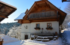 Traditionelles Haus mit Halzbalkon und wei&szlig;er Fassade, umgeben von verschneiter Landschaft.