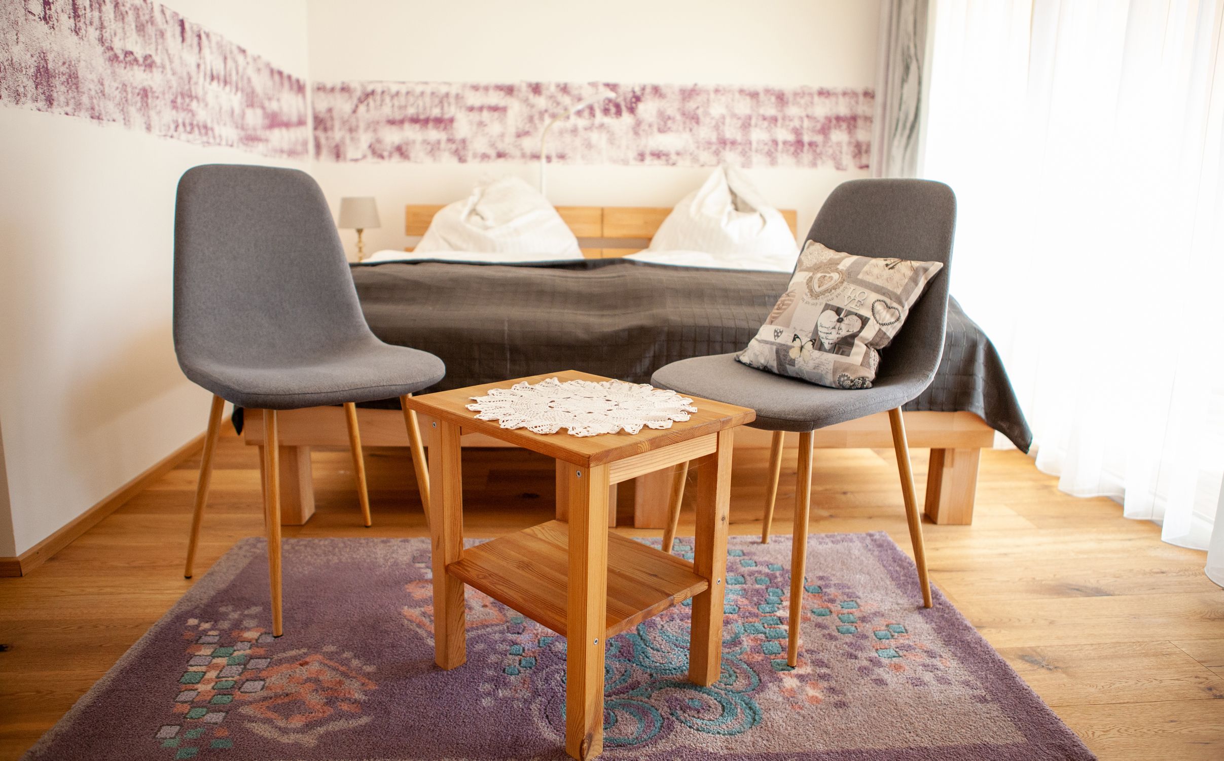 Zwei graue Stühle und ein Holztisch mit Deckchen in einem Schlafzimmer.