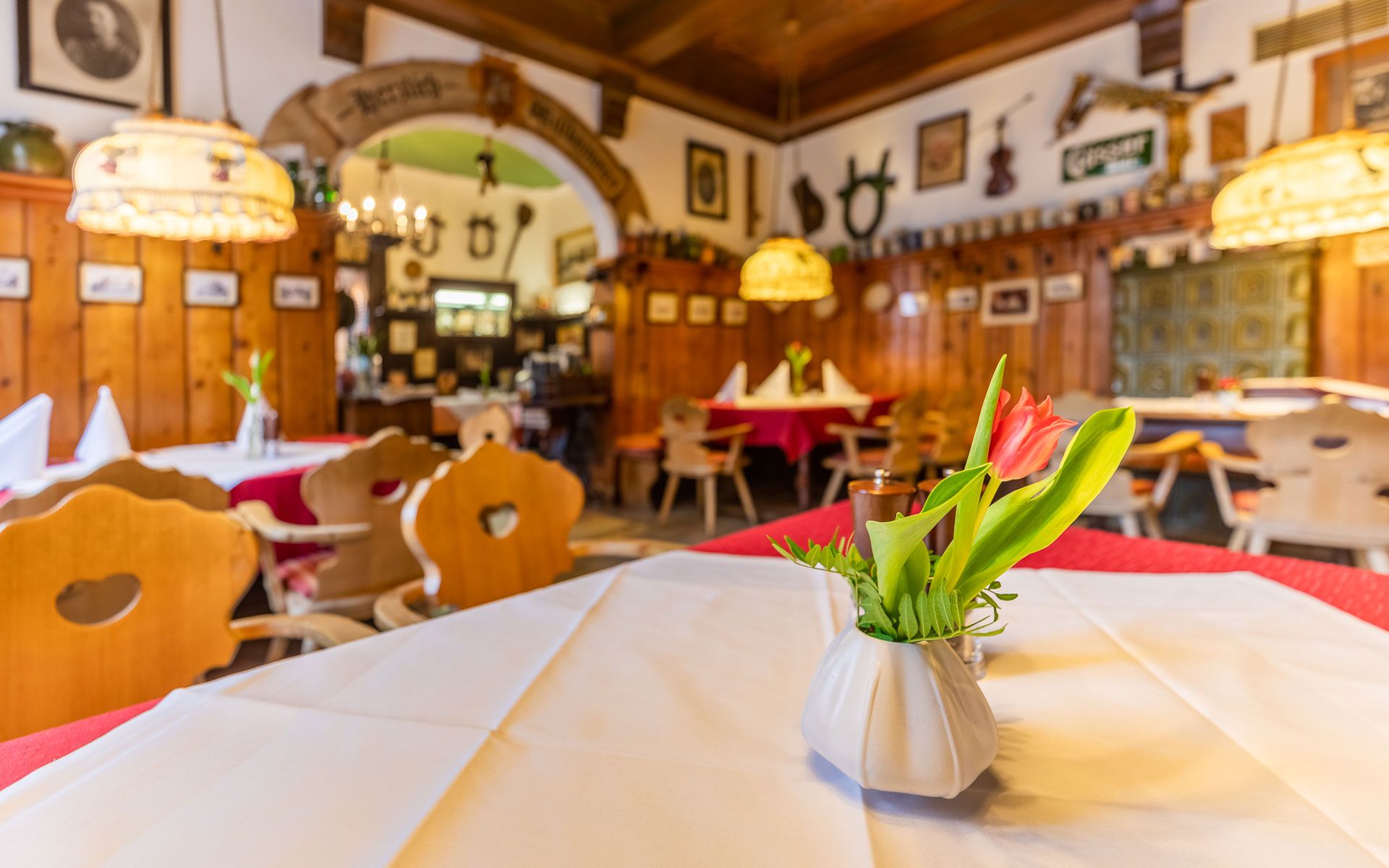 Gemütliches Gastzimmer mit Holzmöbeln, Tischdecken und Blumenvasen.