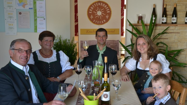 Familie in traditioneller Kleidung sitzt an einem Tisch mit Wein und Gl&auml;sern.