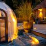 Ein modernes Chalet mit Terrasse und einem transparenten Kuppelzelt im Wald bei Dämmerung.