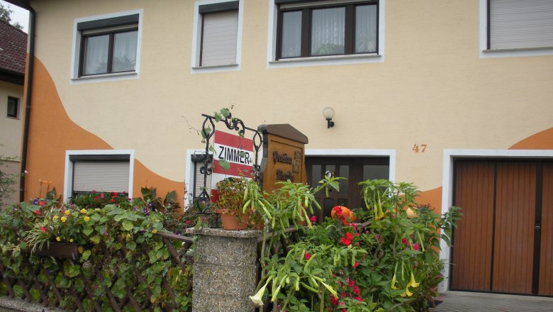 Haus mit gelber Fassade, Blumendekoration und Schild 'Zimmer'.