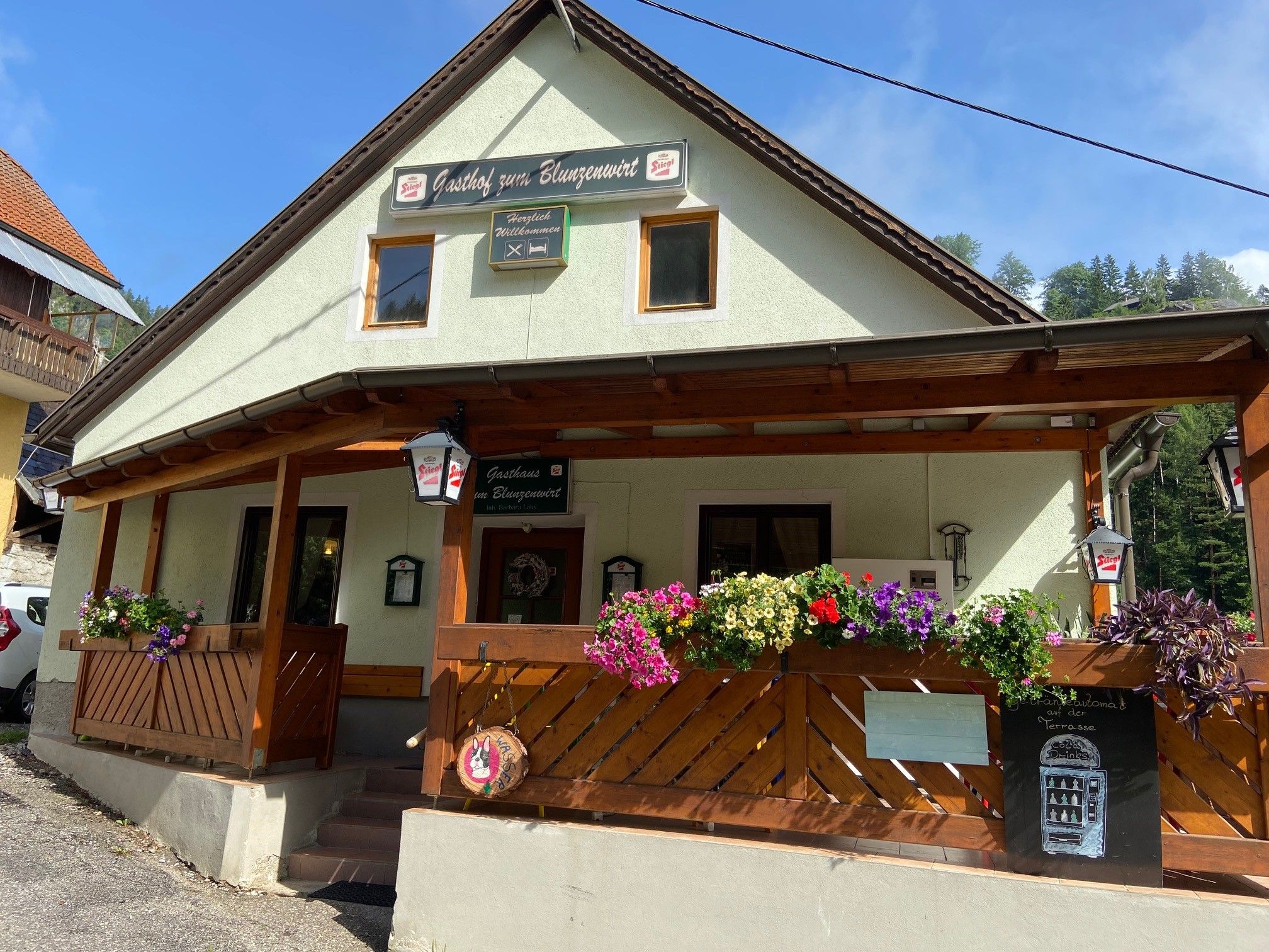Ein traditionelles Gasthaus mit Holzveranda und Blumenkästen, beschriftet als 'Gasthof zum Blunzenwirt'.