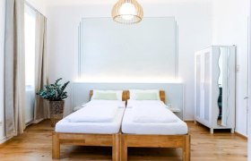 Modernes Gästezimmer mit zwei Einzelbetten, einem Kleiderschrank und einer Pflanze.