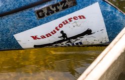 Vorderteil eines Kanus im Wasser mit einem Werbeaufdruck Kanutouren.