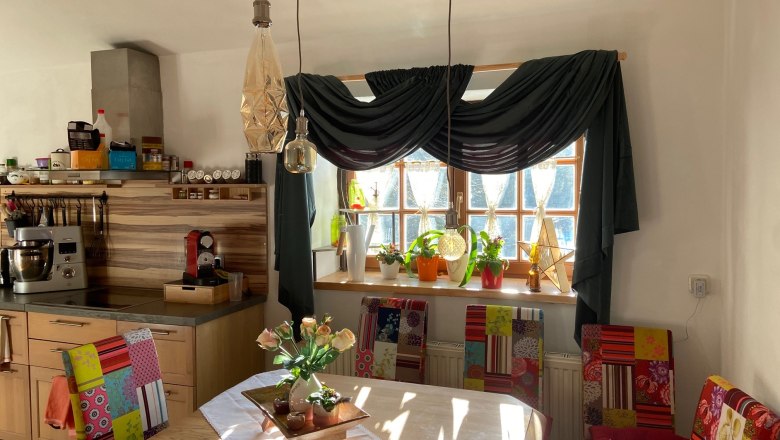 Essbereich mit Holztisch, bunten St&uuml;hlen, Pflanzen auf der Fensterbank und H&auml;ngelampen.