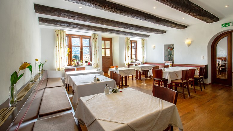 Ein gem&uuml;tlicher Fr&uuml;hst&uuml;cksraum mit Holzbalken, gedeckten Tischen und Blumen auf den Fensterb&auml;nken.