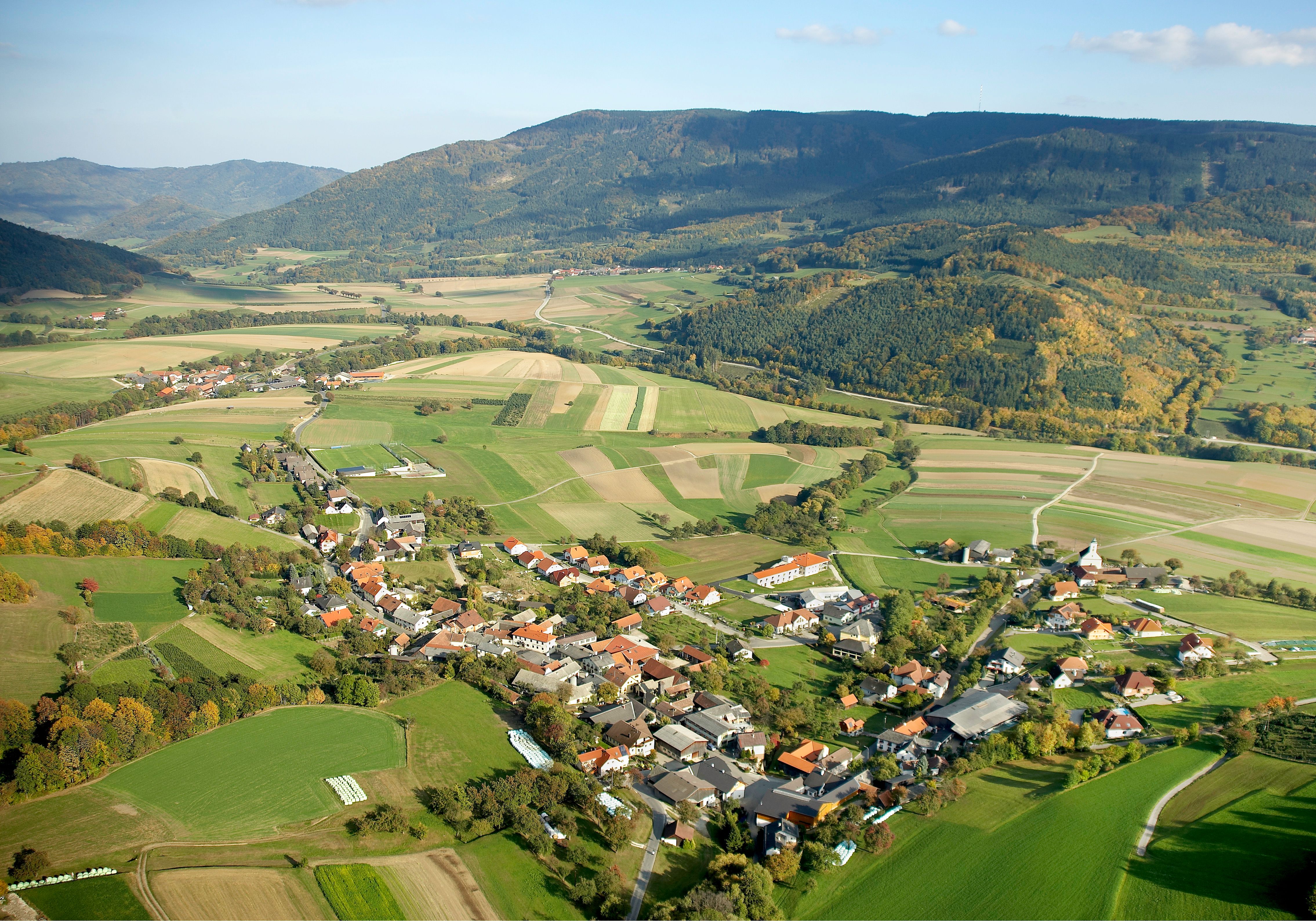 Luftaufnahme einer ländlichen Gemeinde mit Feldern und Hügeln im Hintergrund.