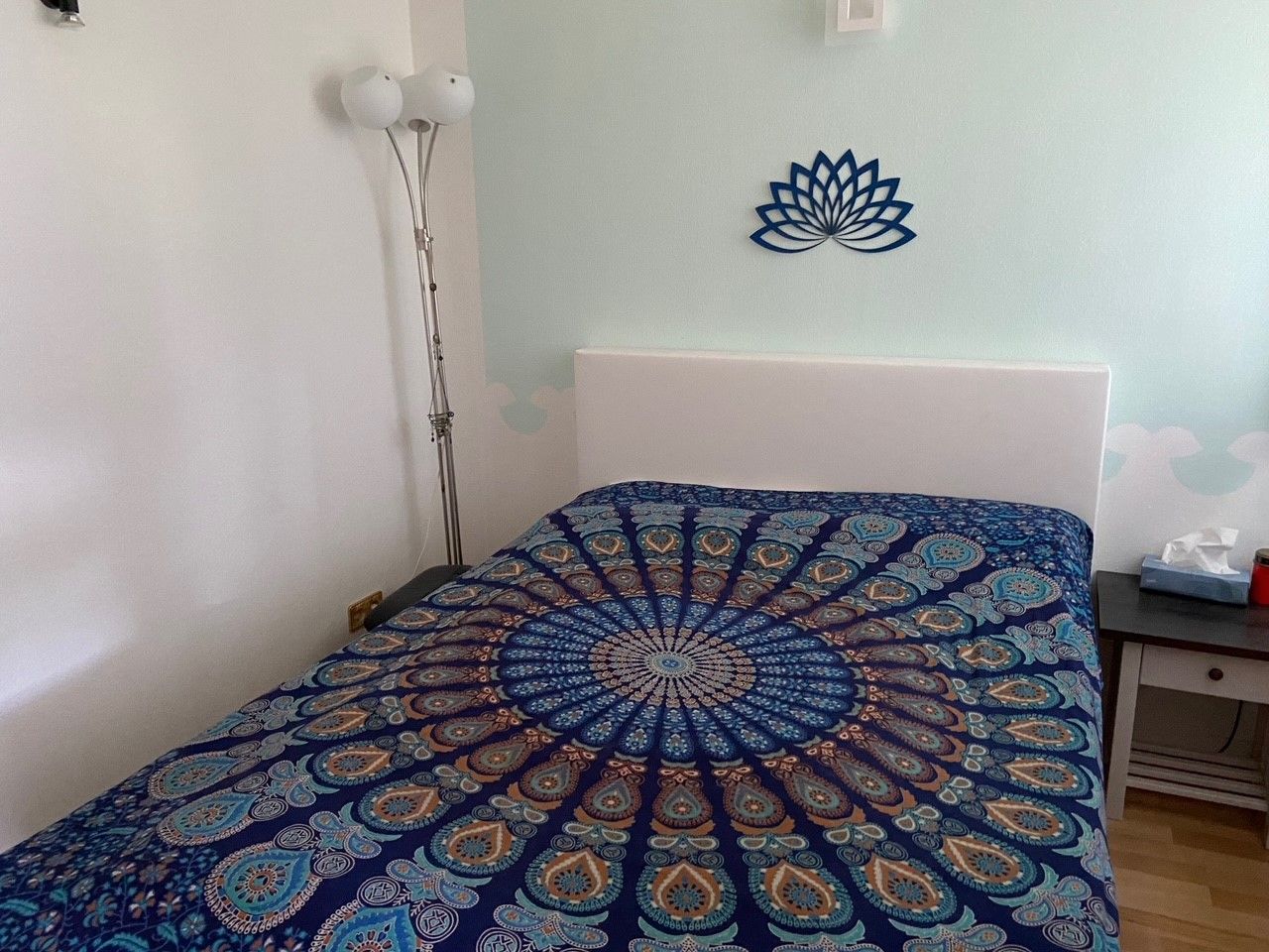 Schlafzimmer mit Wasserbett, bunter Bettdecke und Lotus-Wanddekoration.