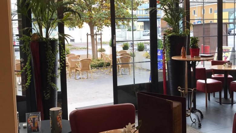 Innenansicht eines Caf&eacute;s mit Blick auf eine Terrasse mit Tischen und St&uuml;hlen.