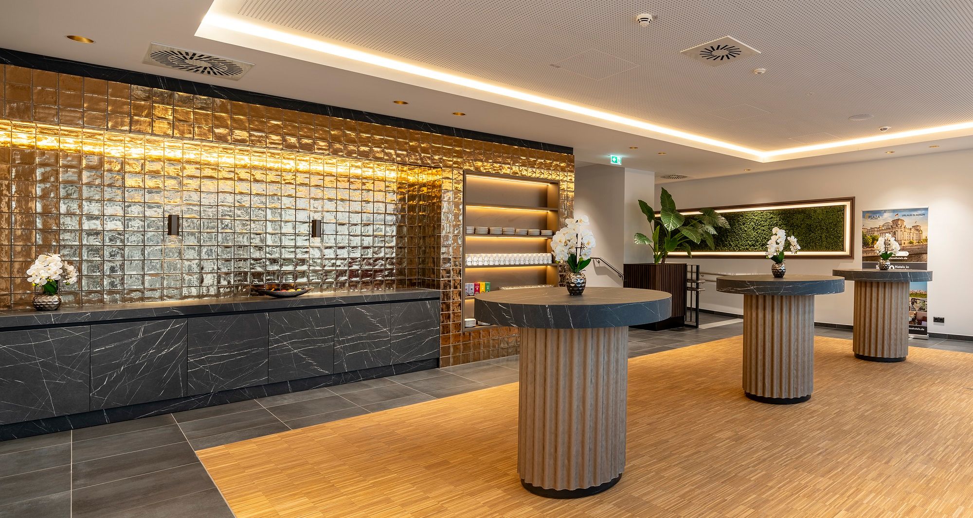 Moderner Raum für Seminar Kaffeepausen mit goldener Wand, schwarzen Marmortischen und Orchideen.