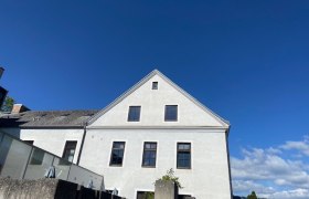 Weißes Gebäude mit Giebeldach vor blauem Himmel.