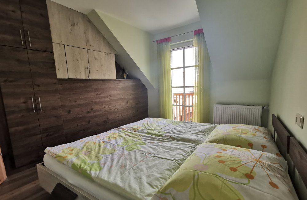 Schlafzimmer mit Doppelbett, Holzschrank und Fenster mit gelben Vorhängen.