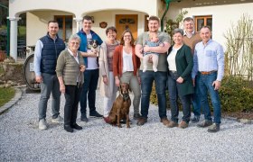 Eine Familie steht vor einem Haus, vier Generationen zusammen mit einem Hund und einem Baby.