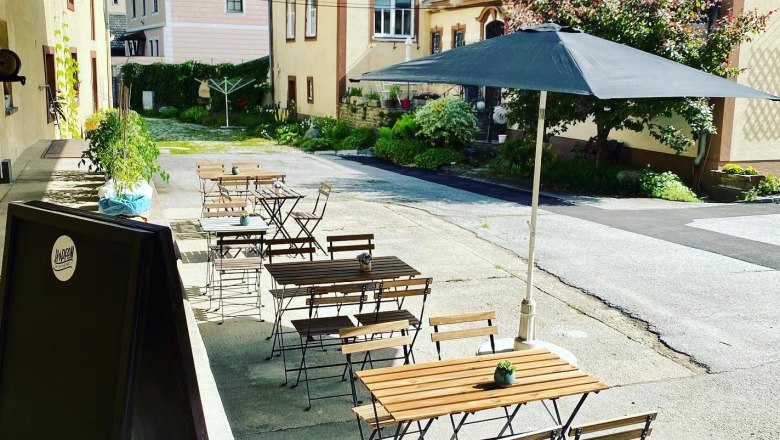 Ein Gastgarten mit Holztischen und Stühlen, einem Sonnenschirm und Pflanzen in einem Innenhof.