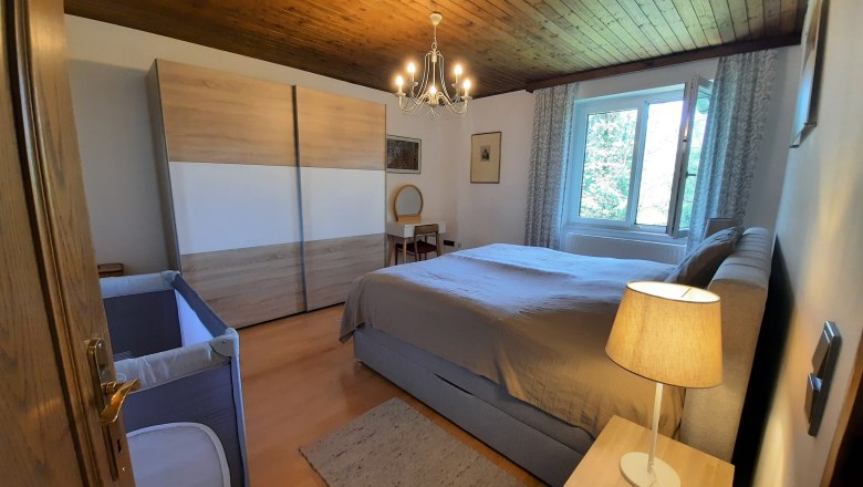Ein gem&uuml;tliches Schlafzimmer mit Holzboden, Doppelbett, Kleiderschrank, Kinderbett und Nachttischlampe.