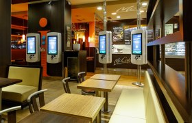 Innenansicht eines McDonald's Restaurants mit Bestellterminals und Sitzbereichen.