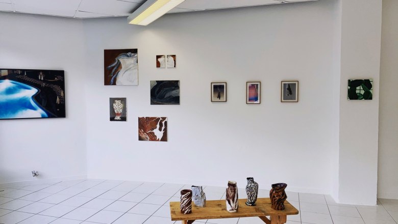 Galerieraum mit Kunstwerken an der Wand und Keramiken auf einem Holztisch.