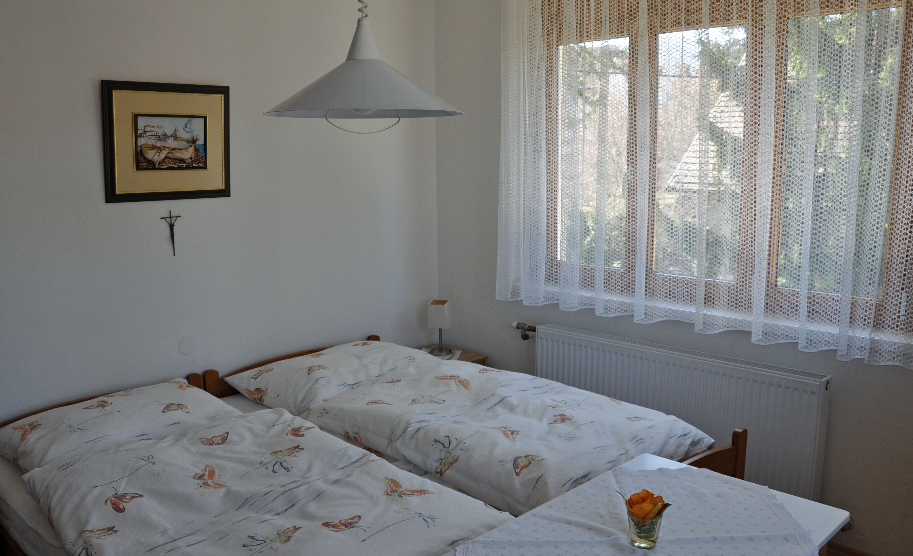 Gemütliches Schlafzimmer mit zwei Einzelbetten, einem Bild an der Wand und einem Fenster mit Spitzenvorhang.