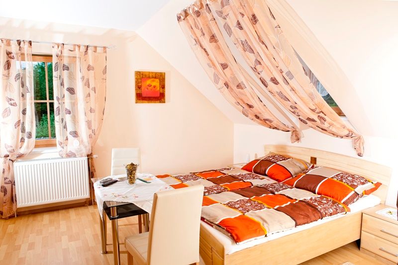 Helles Schlafzimmer mit Doppelbett, Tisch und Stühlen, dekoriert mit Vorhängen und einem Bild an der Wand.