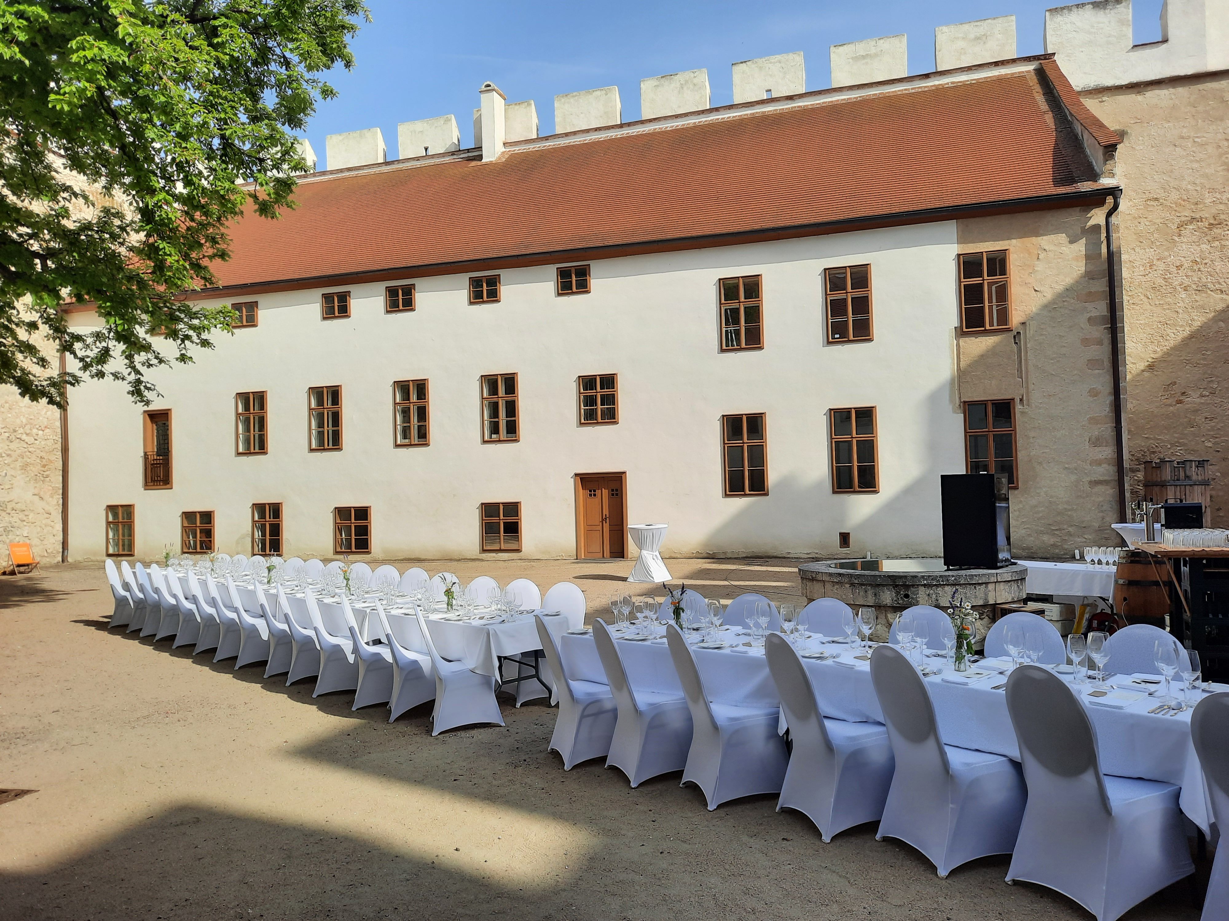 Langer Tisch mit weißen Stühlen in einem historischen Innenhof.