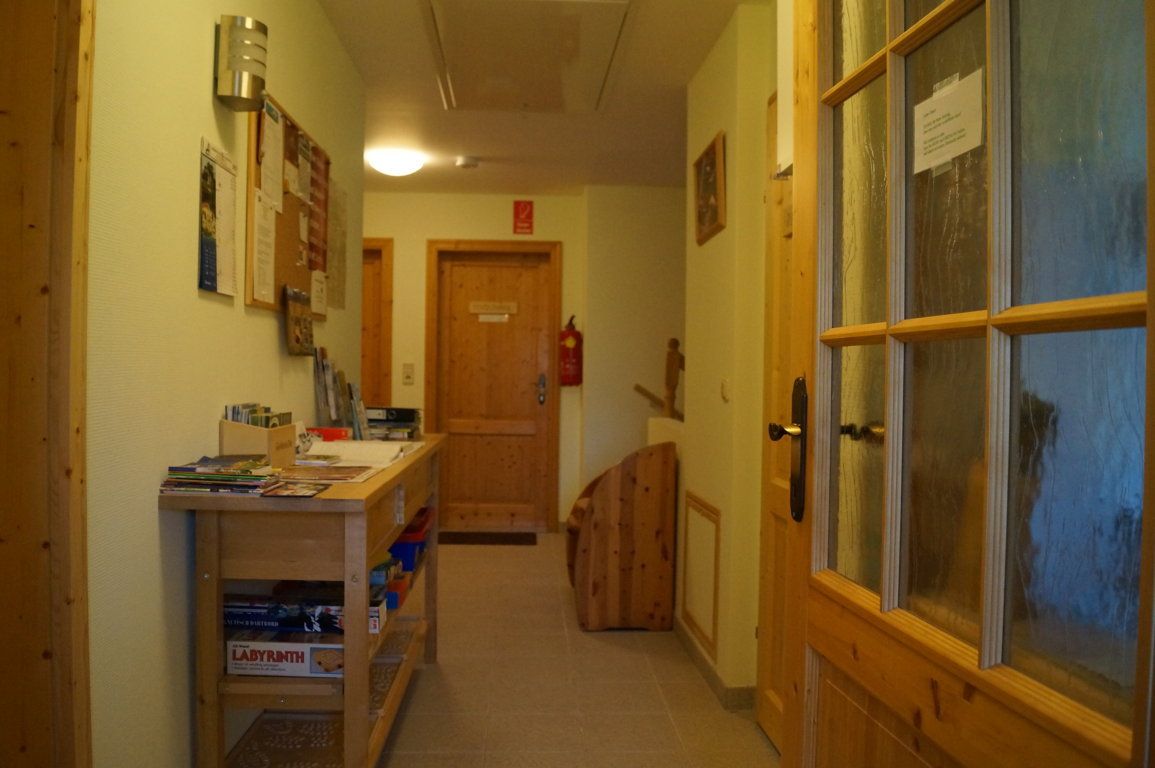 Ein Flur mit Holztüren, einem Tisch mit Broschüren und Spielen, und einer Pinnwand an der Wand.