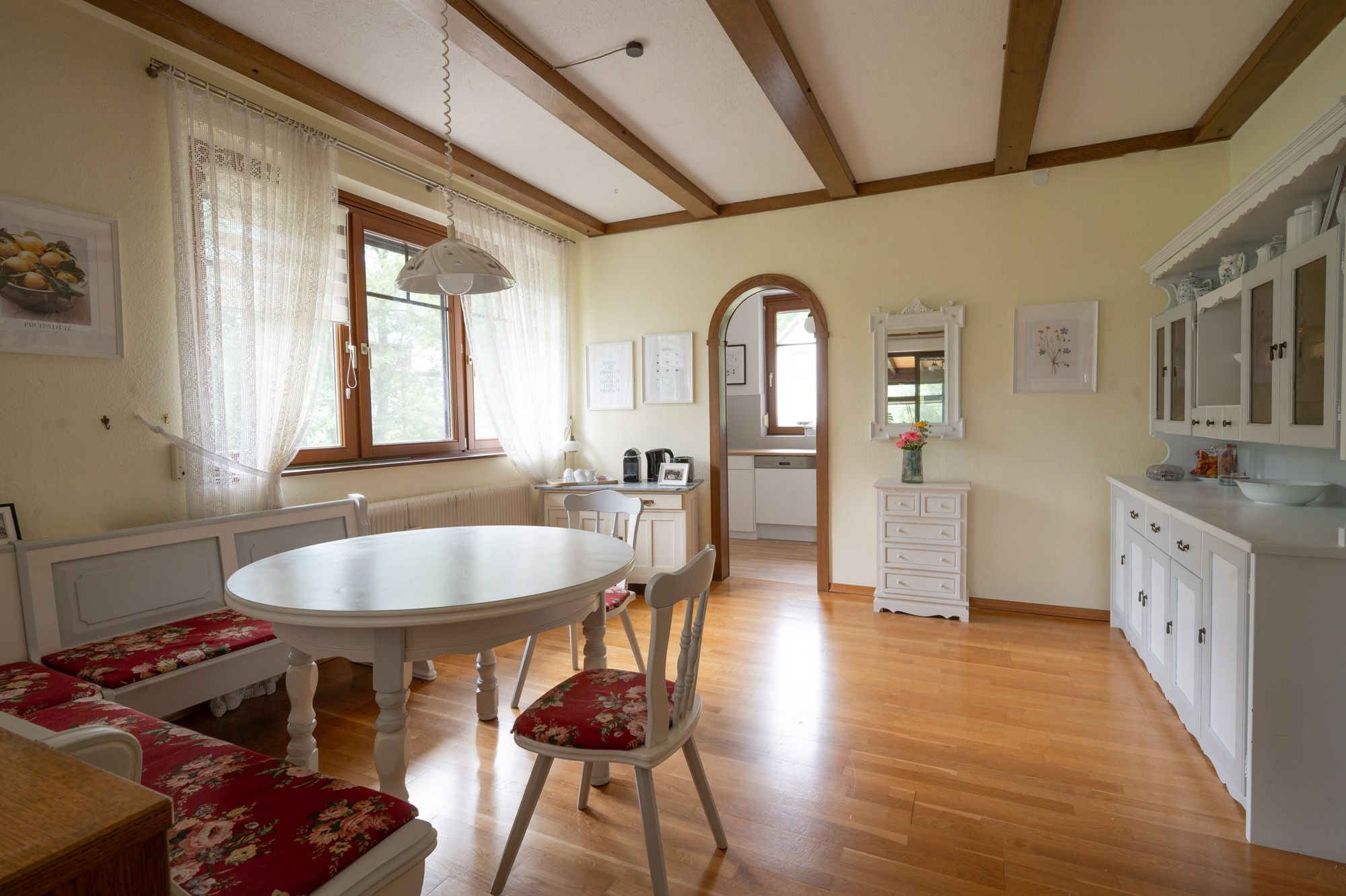 Essbereich in einem Ferienhaus mit Holzboden, weißen Möbeln und roten Polstern.