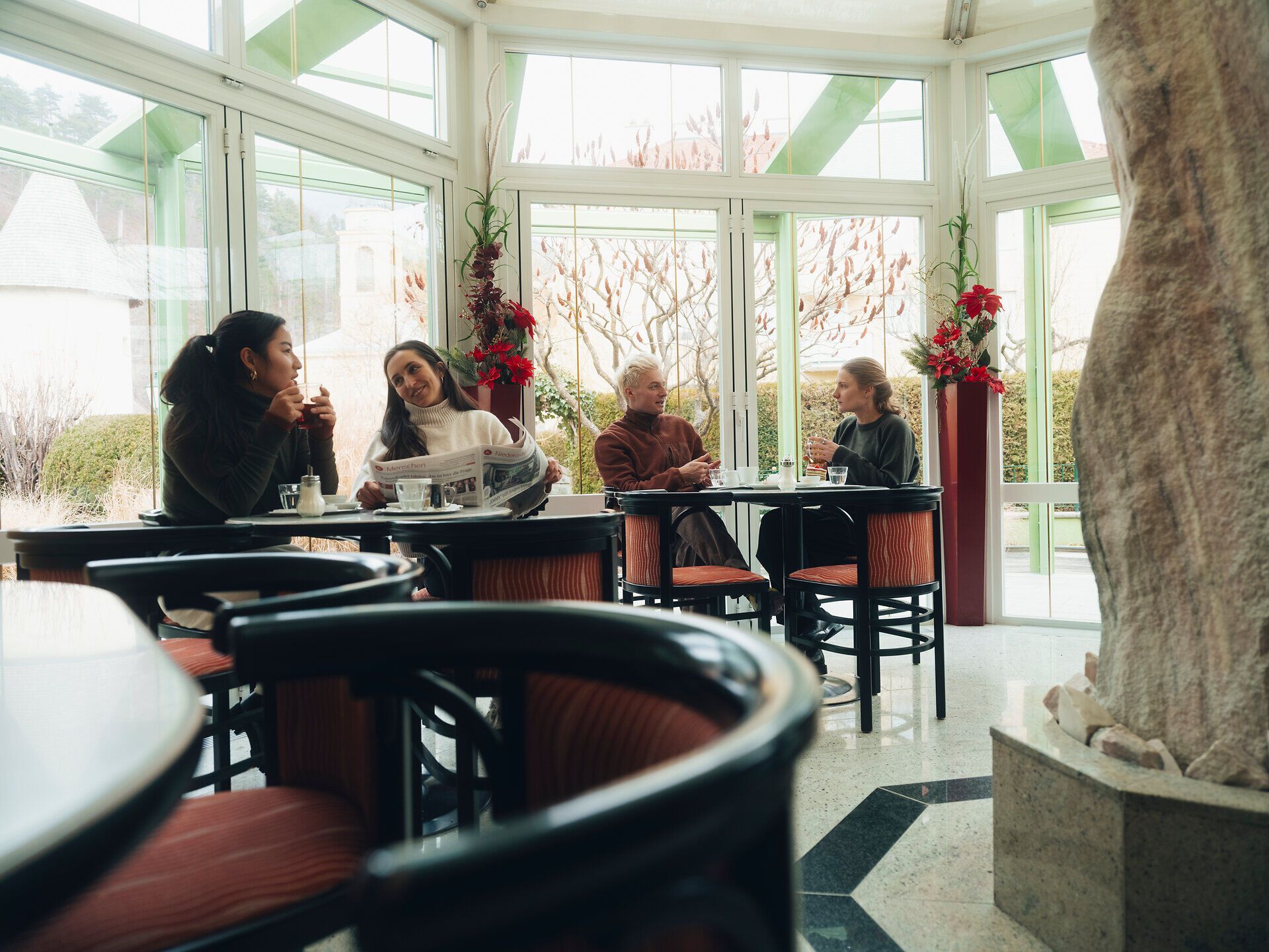 In der gemütlichen Atmosphäre der Konditorei Nöbauer genießen die Gäste köstliche Leckereien und anregende Gespräche. Die großen Fenster bieten einen herrlichen Blick auf die winterliche Landschaft der Wiener Alpen, während die warmen Farben des Interieurs eine einladende Stimmung schaffen.