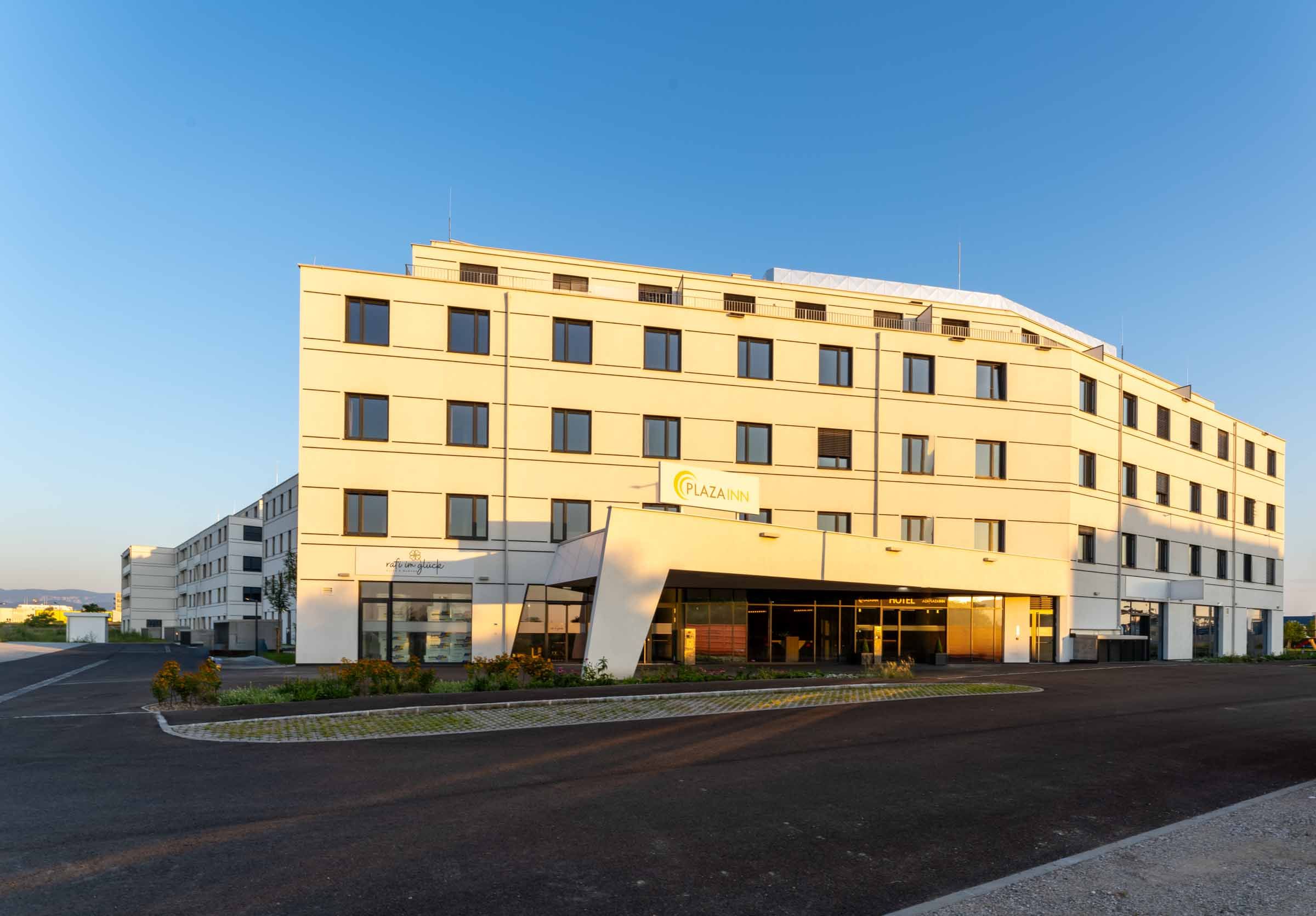 Ein modernes, mehrstöckiges Gebäude mit der Aufschrift 'Plaza INN' bei Sonnenuntergang.