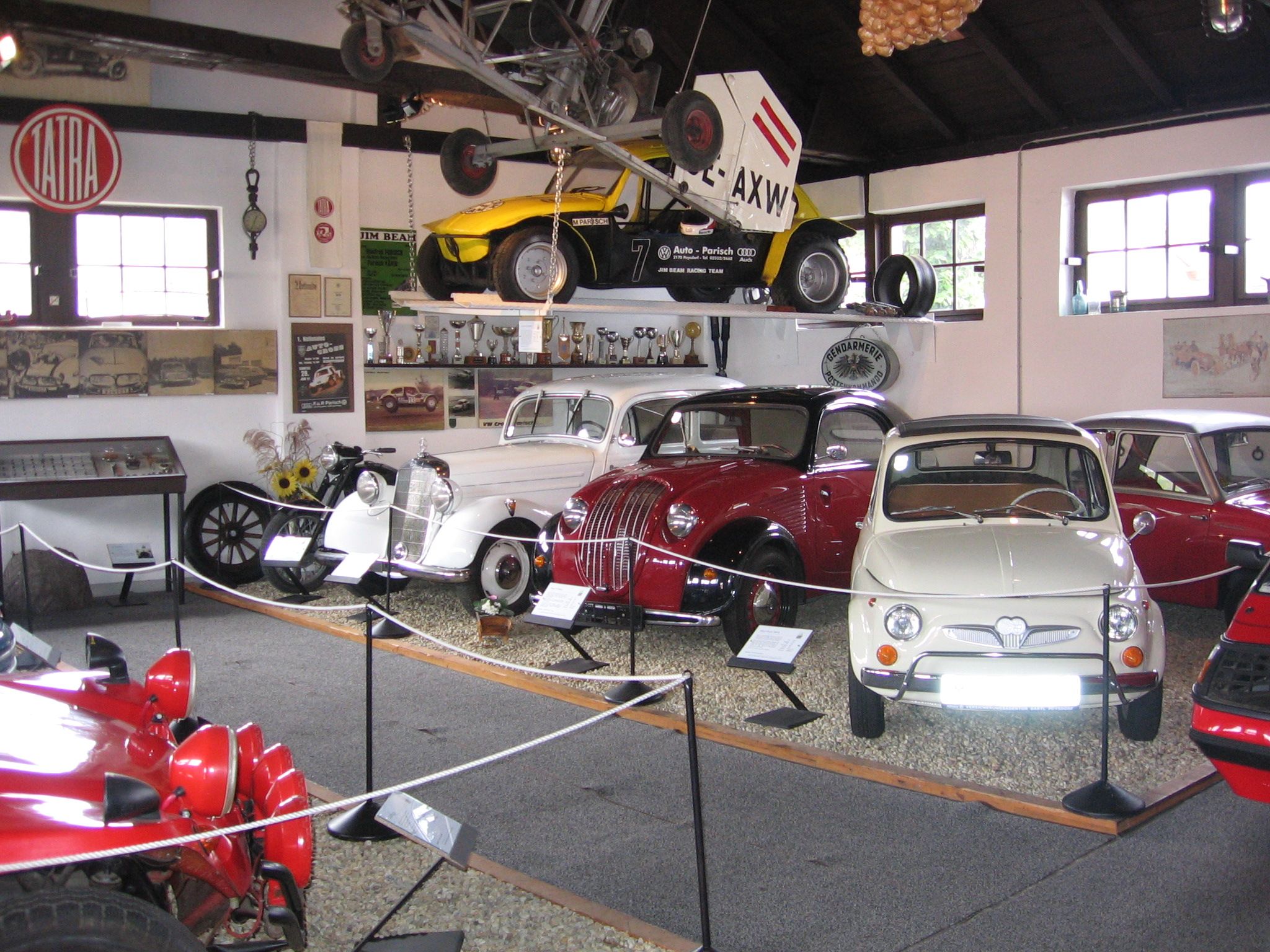 Innenansicht eines Oldtimermuseums mit verschiedenen klassischen Autos und einem Flugzeug an der Decke.