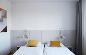 Modernes Gästezimmer mit zwei Einzelbetten, gelben Kissen und Wandlampen.